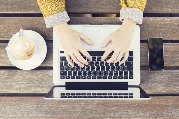Typing girl with laptop, smartphone and coffee mug